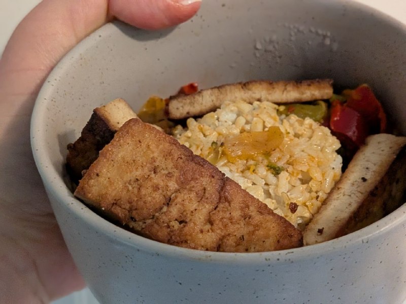 A picture of a bowl of rice with peppers, onions, broccoli, and fried tofu set around it